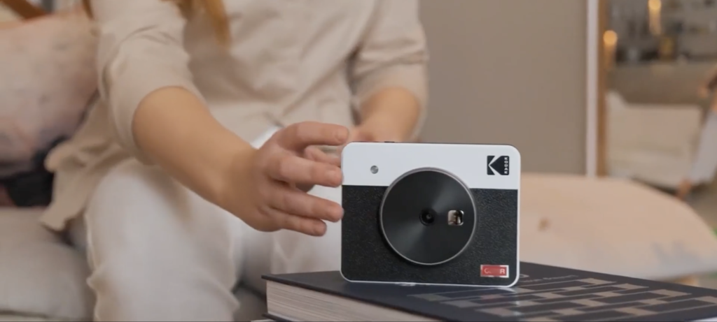 Someone reaching for the Kodak Mini Shot 3 camera on a table, from a video on their Amazon page