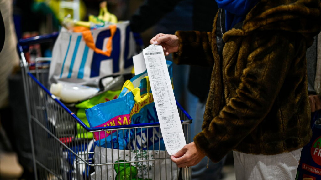Shopper holding a long grocery receipt beside a full cart.