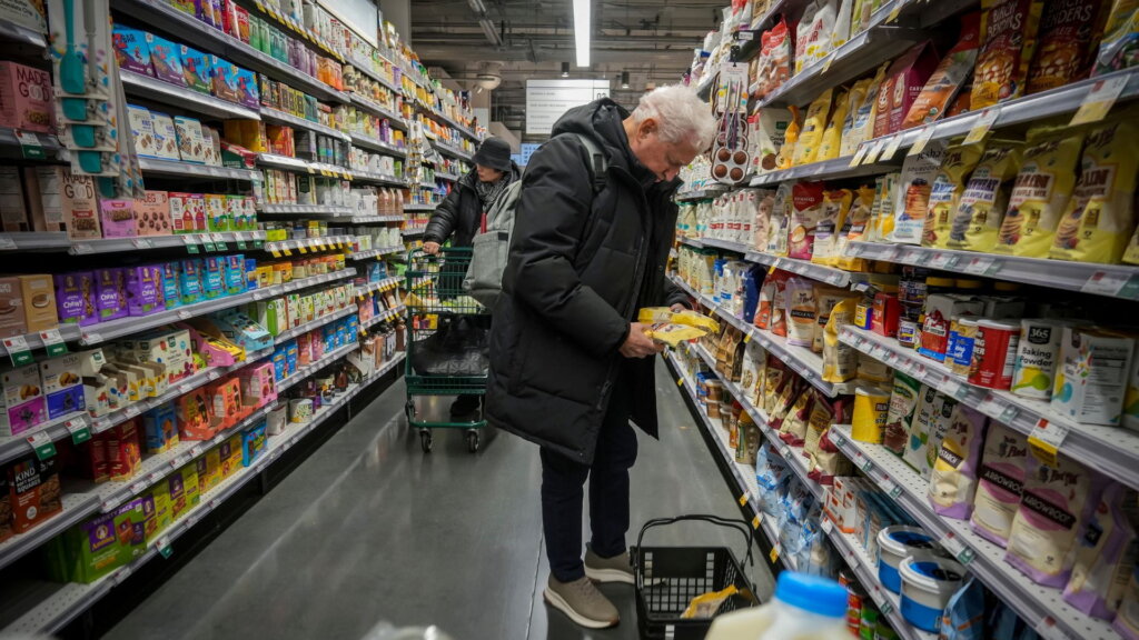 Older shopper reading a package label in a grocery aisle.