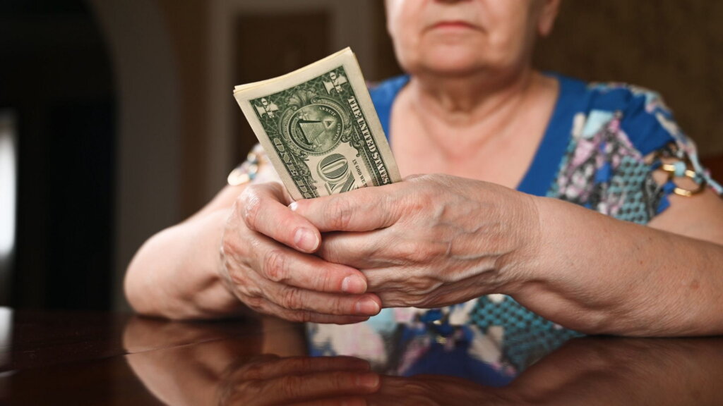 Older woman holding a small stack of dollar bills.