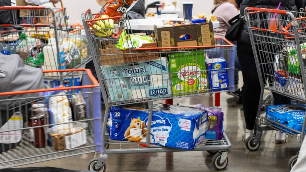 Loaded warehouse store cart with paper towels and bath tissue.